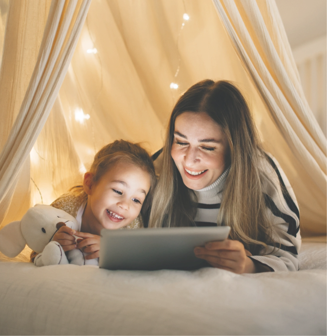 Mutter und Tochter schauen gemeinsam auf ein Tablet im Bett.